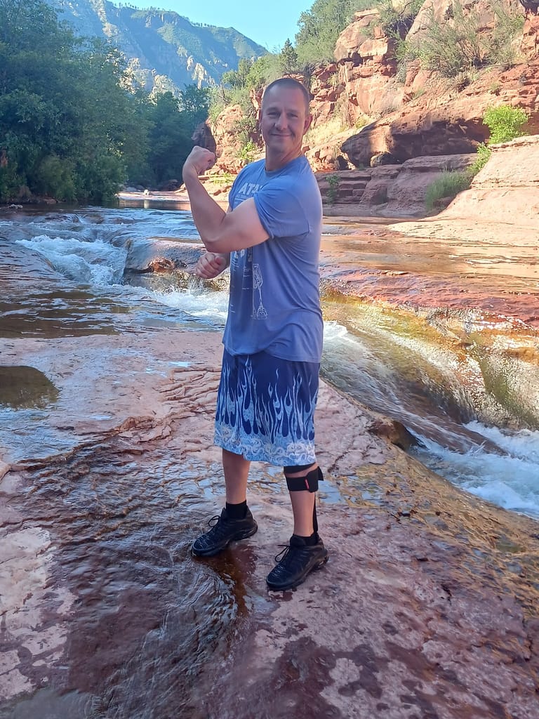 Tyson Dale smiling and flexing his arm beside a rocky creek